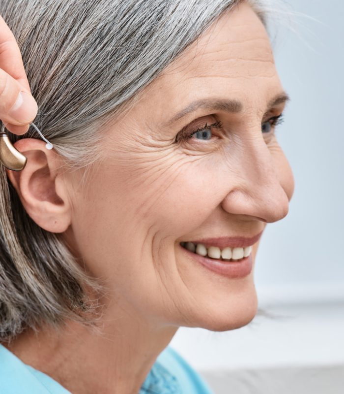 Close-up of hearing aid near senior female patient's ear at audiology clinic. Hearing solutions, hearing BTE aids